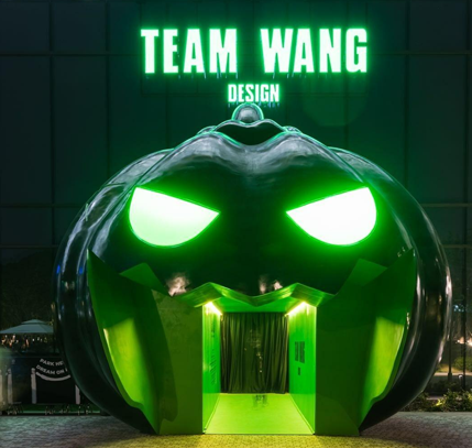 Giant illuminated green pumpkin installation beneath TEAM WANG DESIGN signage