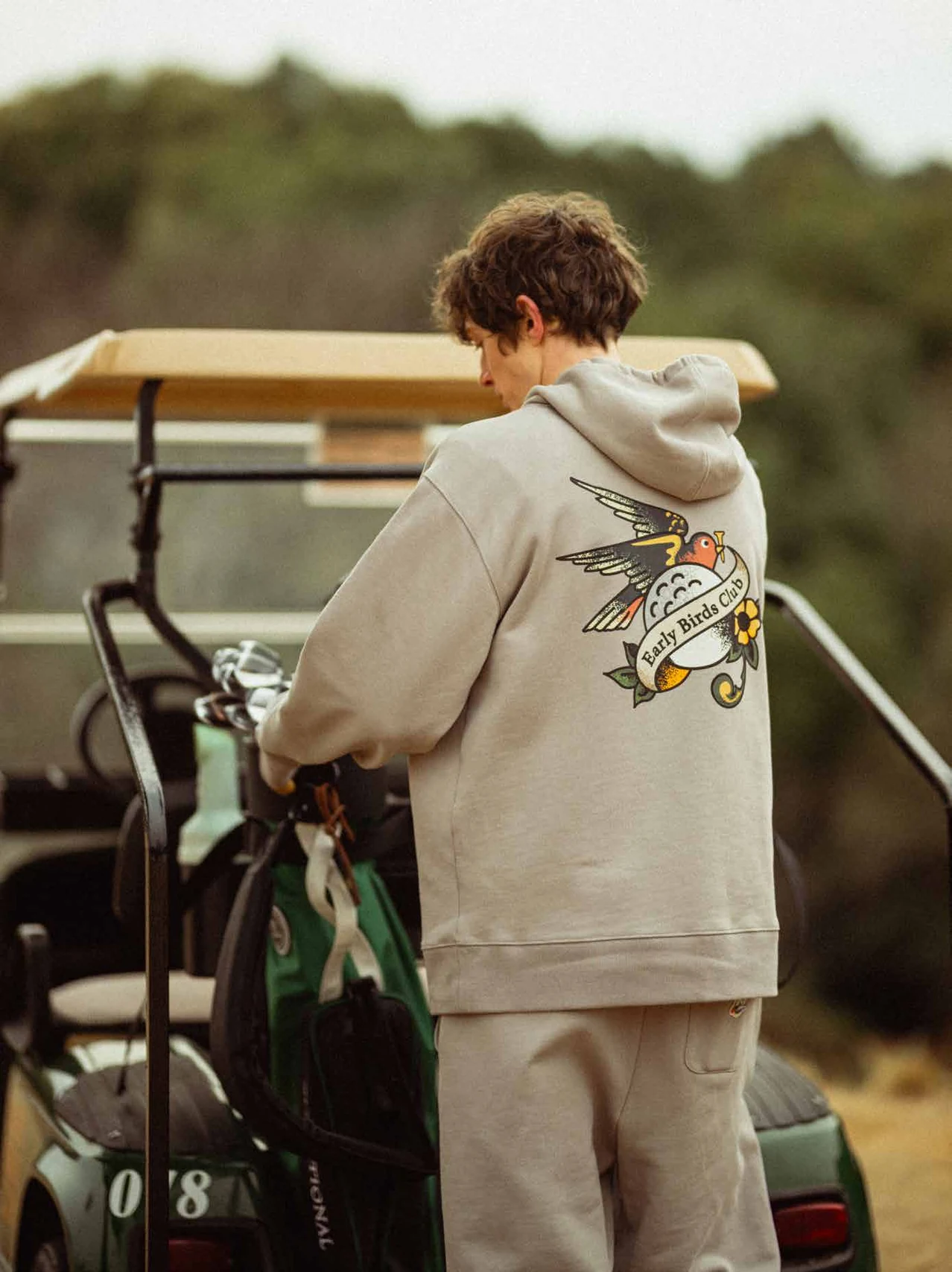 Model in a grey illustrated hoodie standing beside a golf cart